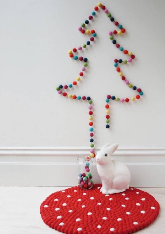 Des pompons colorés contournent le dessin de l'arbre sur le mur